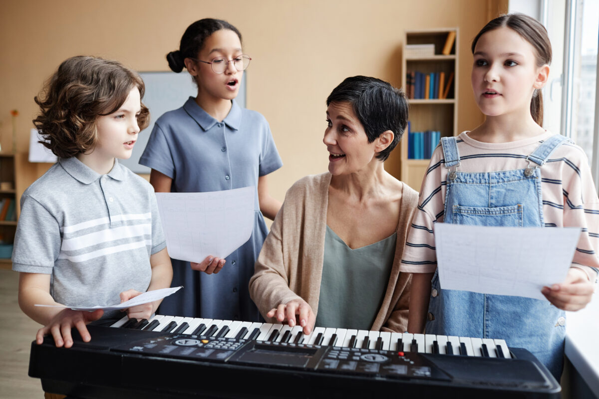 Group of voice students singing while teacher plays piano